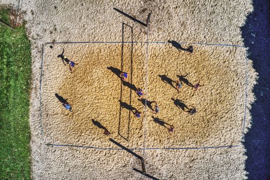 Drone shot capturing an active beach volleyball game from above on a sunny day.