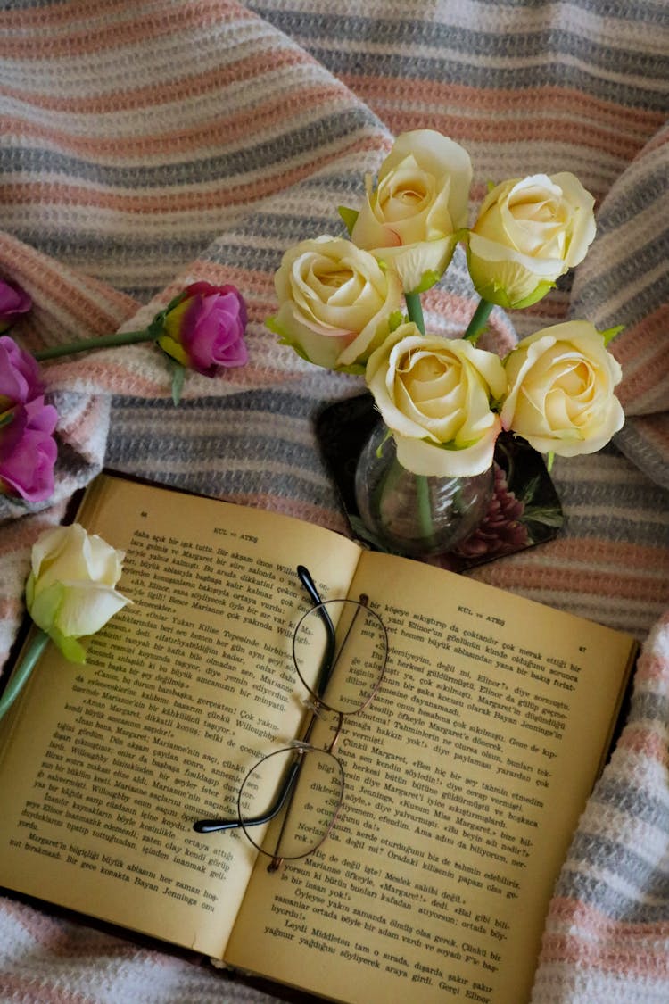 Glasses Laying On Open Book With Pink And Creamy Roses Around