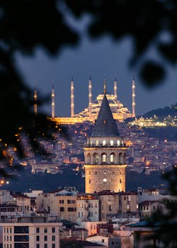 Night view of Istanbul's iconic Galata Tower and Suleymaniye Mosque illuminated against the city skyline.