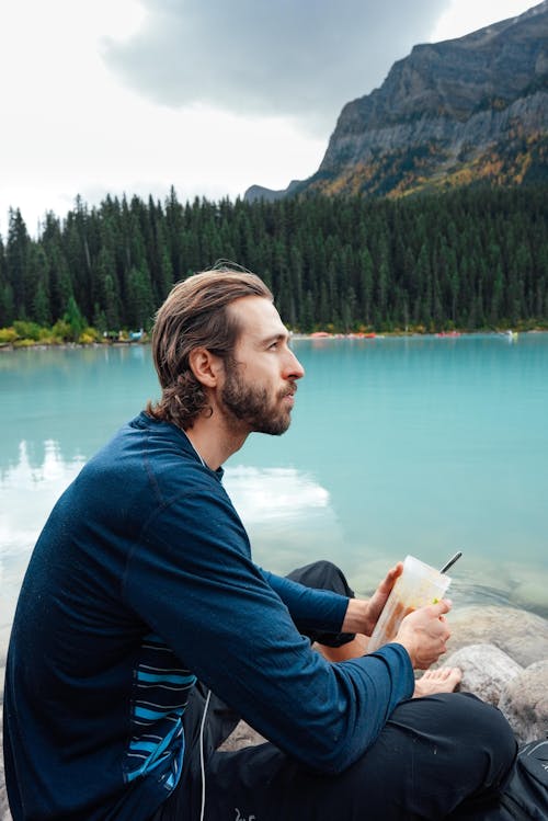 Side View of a Man in a Blue Long Sleeve Shirt Sitting Near a River