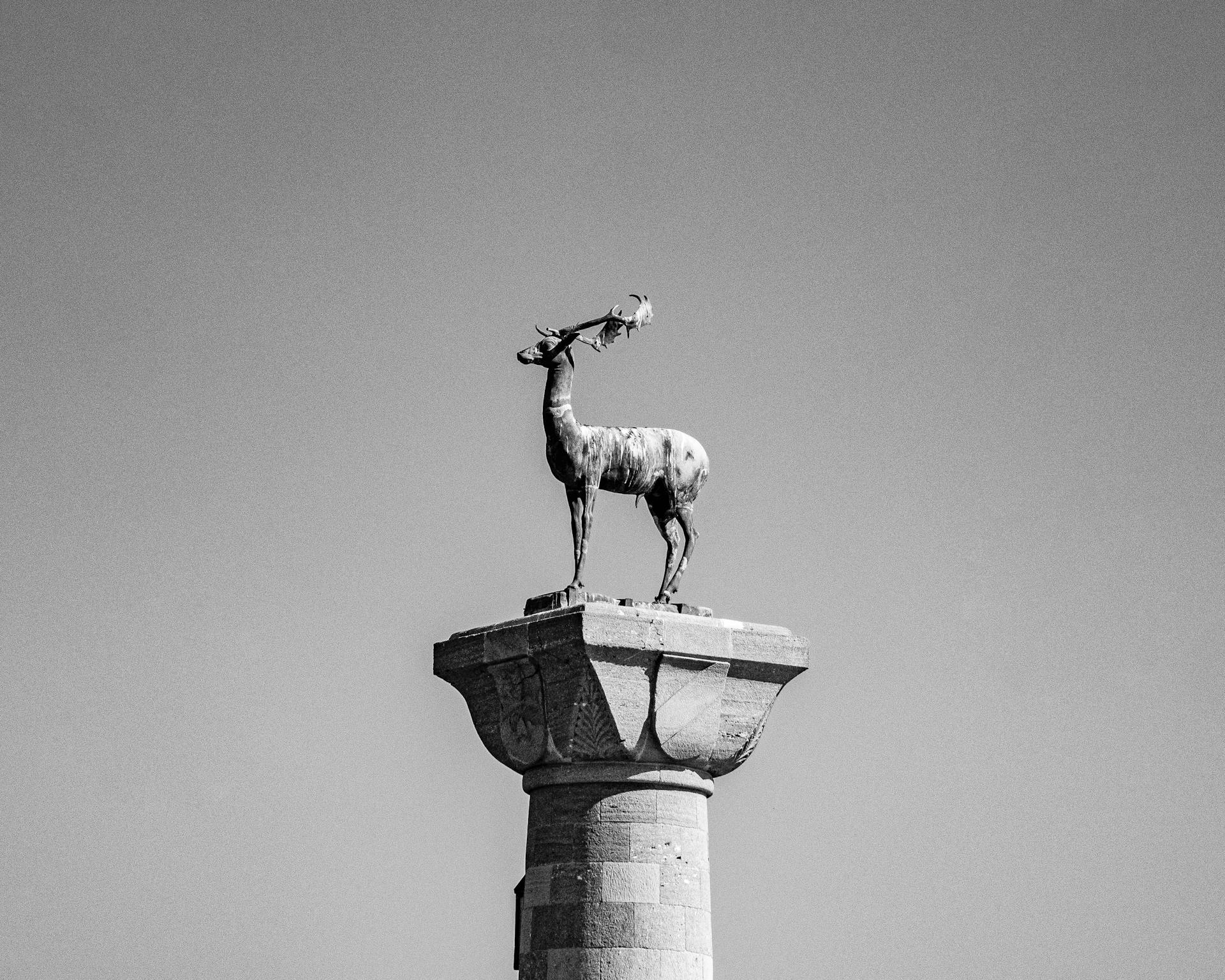 Black and white photo of the Rhodes deer sculpture on a column under a clear sky.