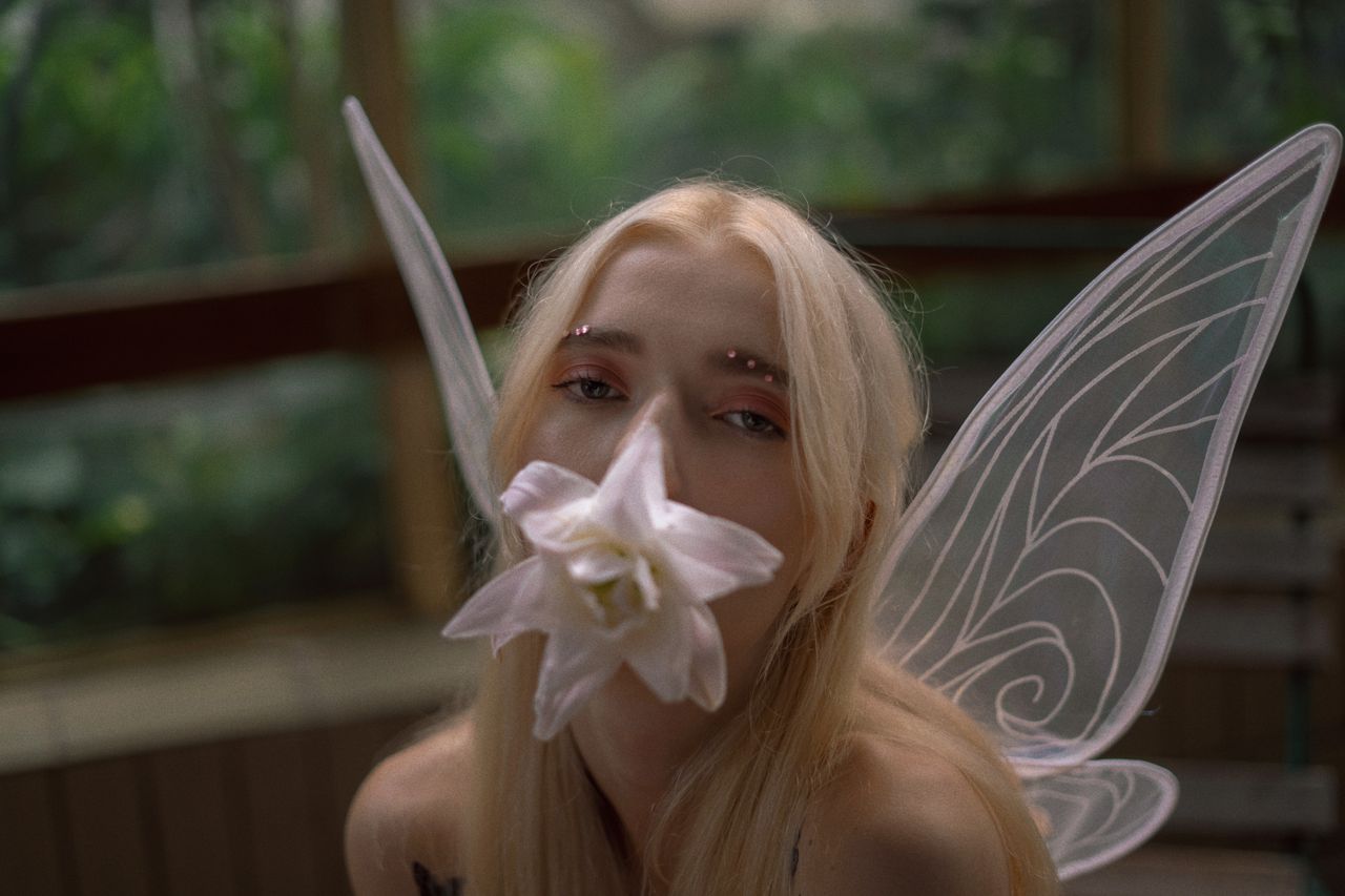 a magical fairy with wings holding a large white flower set in a lush