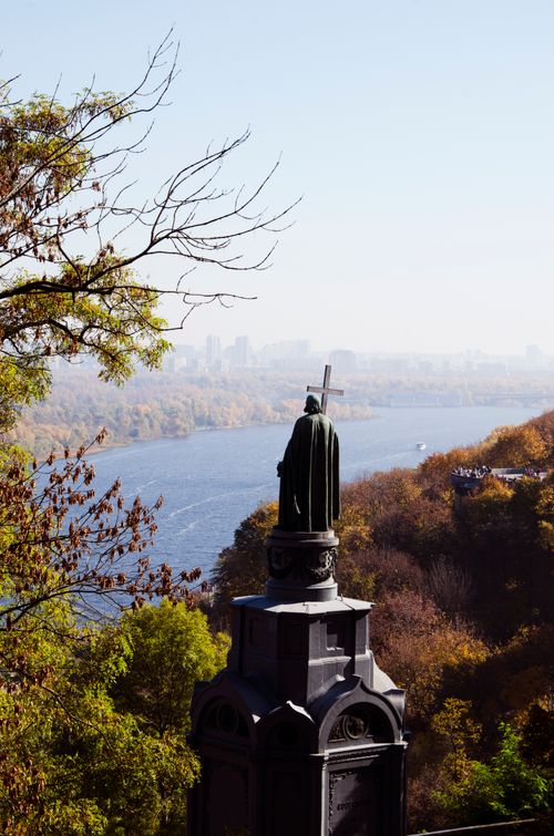 Free Statue with Cross Overlooks a River Amidst Vibrant Autumn Foliage. Stock Photo