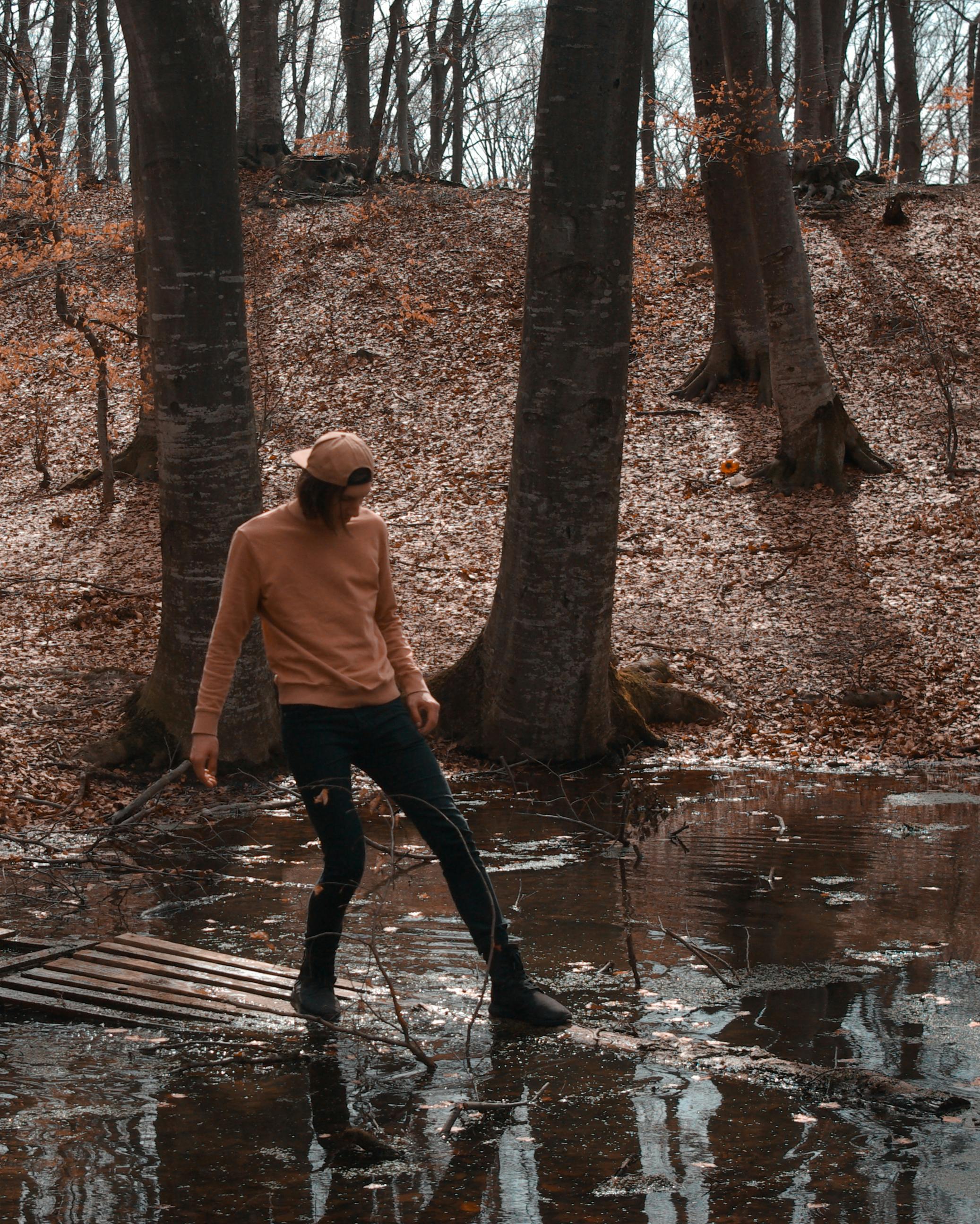 在宁静的秋日森林里，一位穿着休闲服装的年轻人站在池塘边