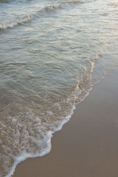 Free Gentle waves lapping the sandy shore at sunset, capturing tranquility and nature's beauty. Stock Photo