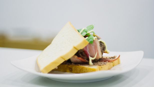 Mouthwatering sandwich with bread, meat, herbs, and sauce on a white plate.