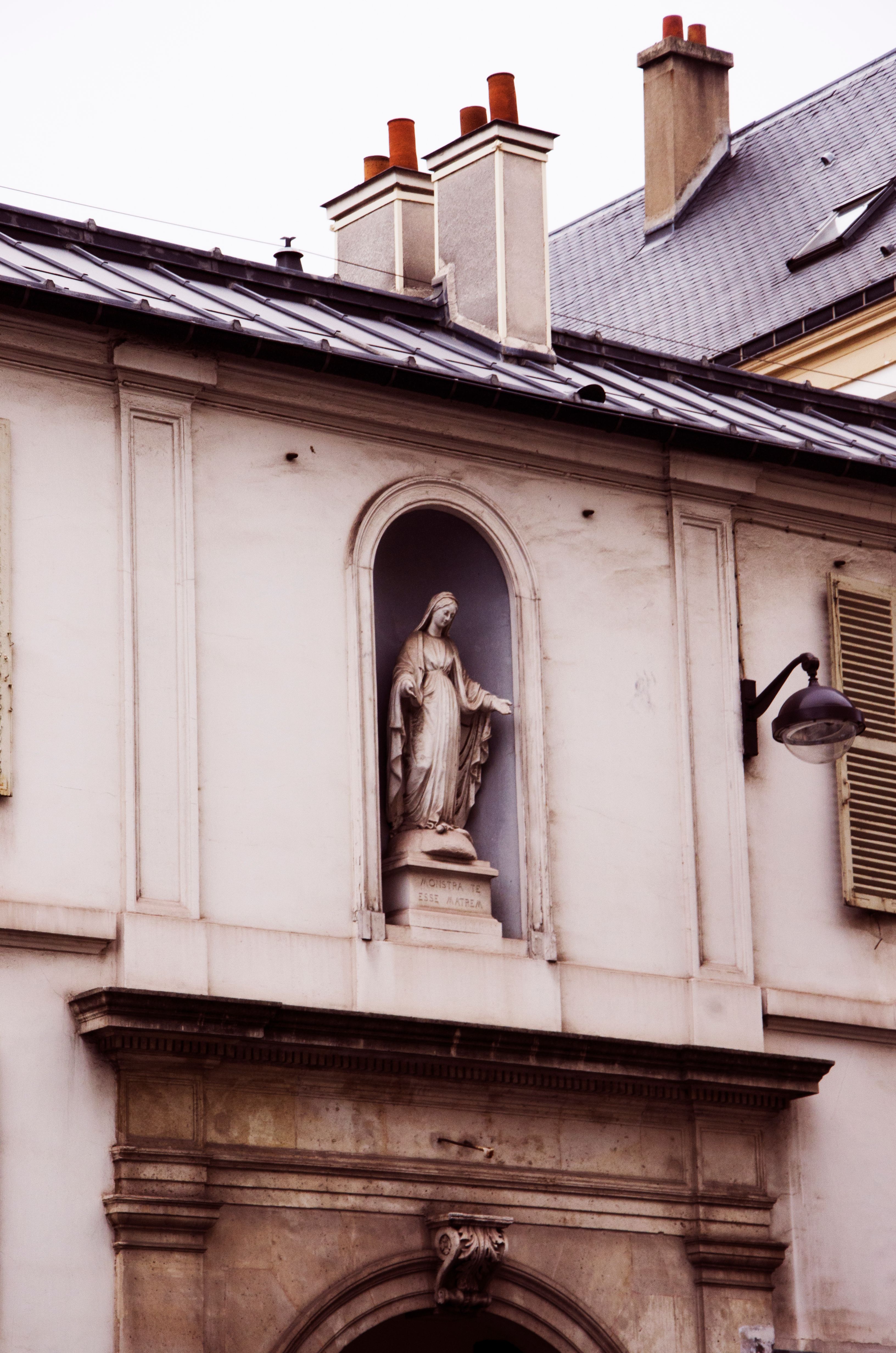 Statue of Virgin Mary on facade of historical building with architectural details.