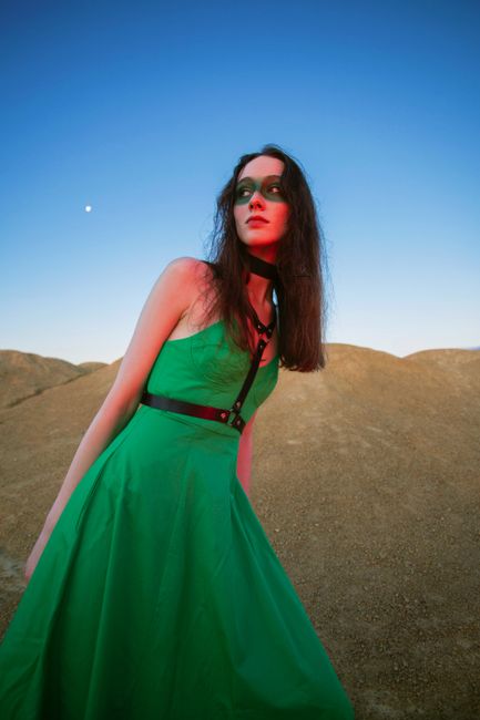 Fashion portrait of a woman in a green dress with bold makeup under a clear sky.