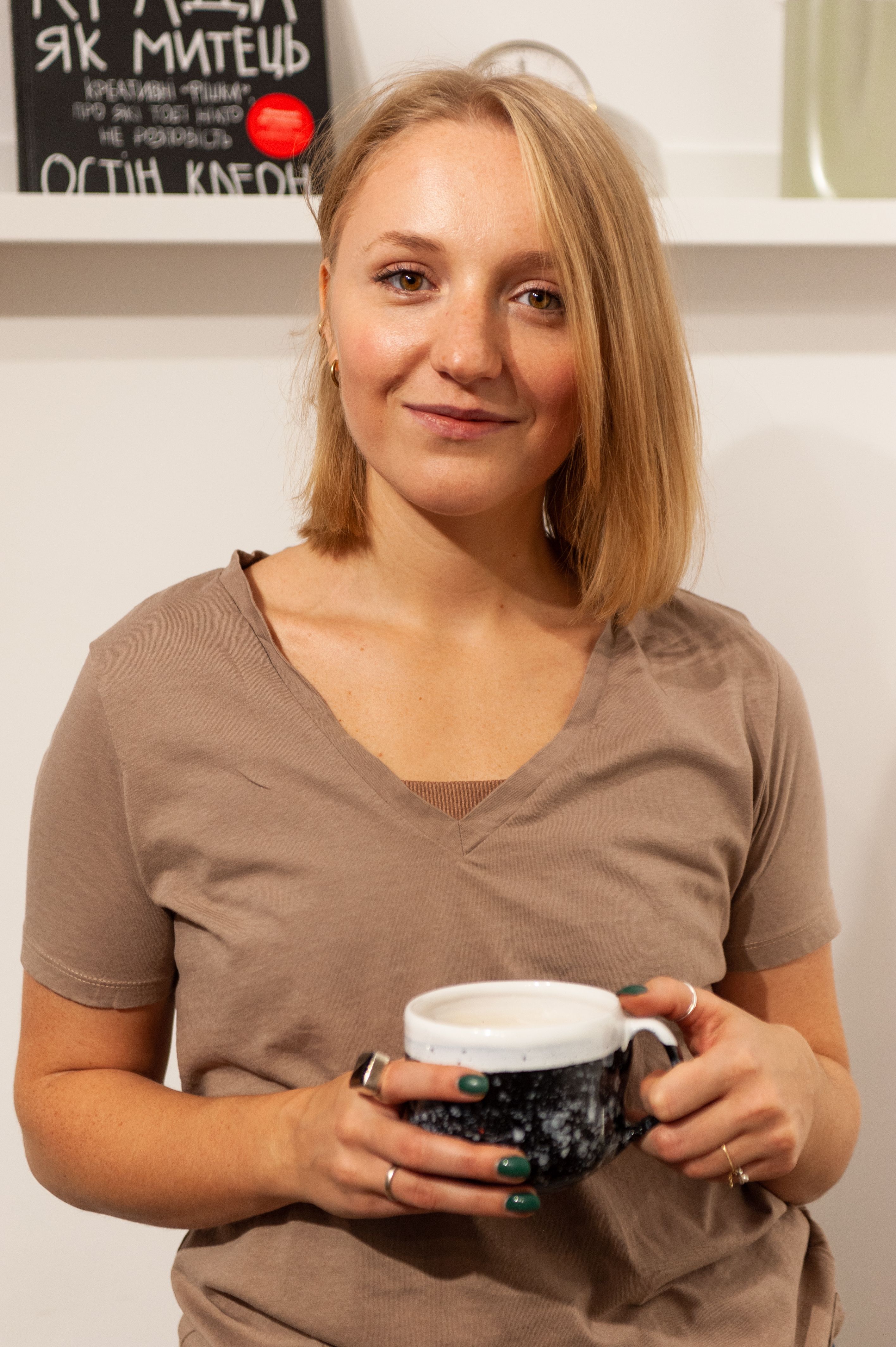 Smiling woman with blond hair holding a mug in a cozy indoor setting.