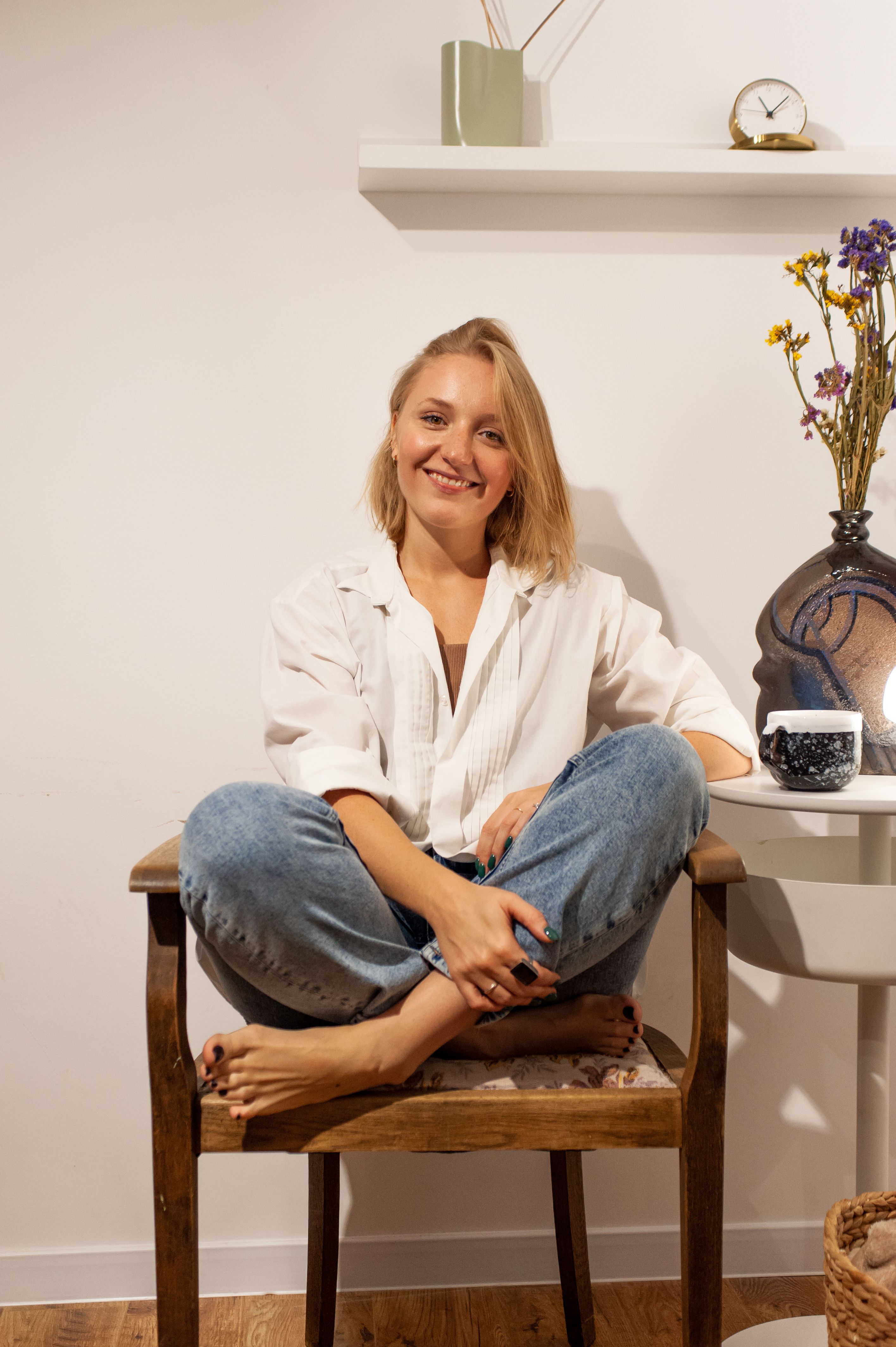 Young woman sitting cross-legged on a chair, smiling in a cozy home setting.