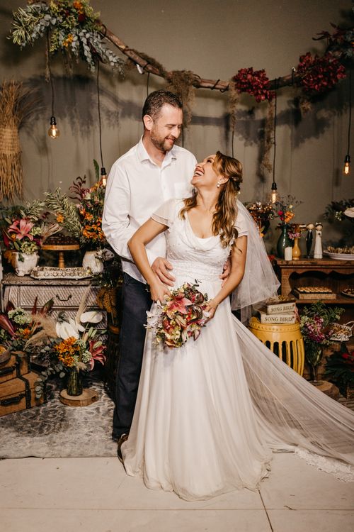 Free Smiling bride and groom in a rustic wedding setup adorned with flowers and warm lights. Stock Photo