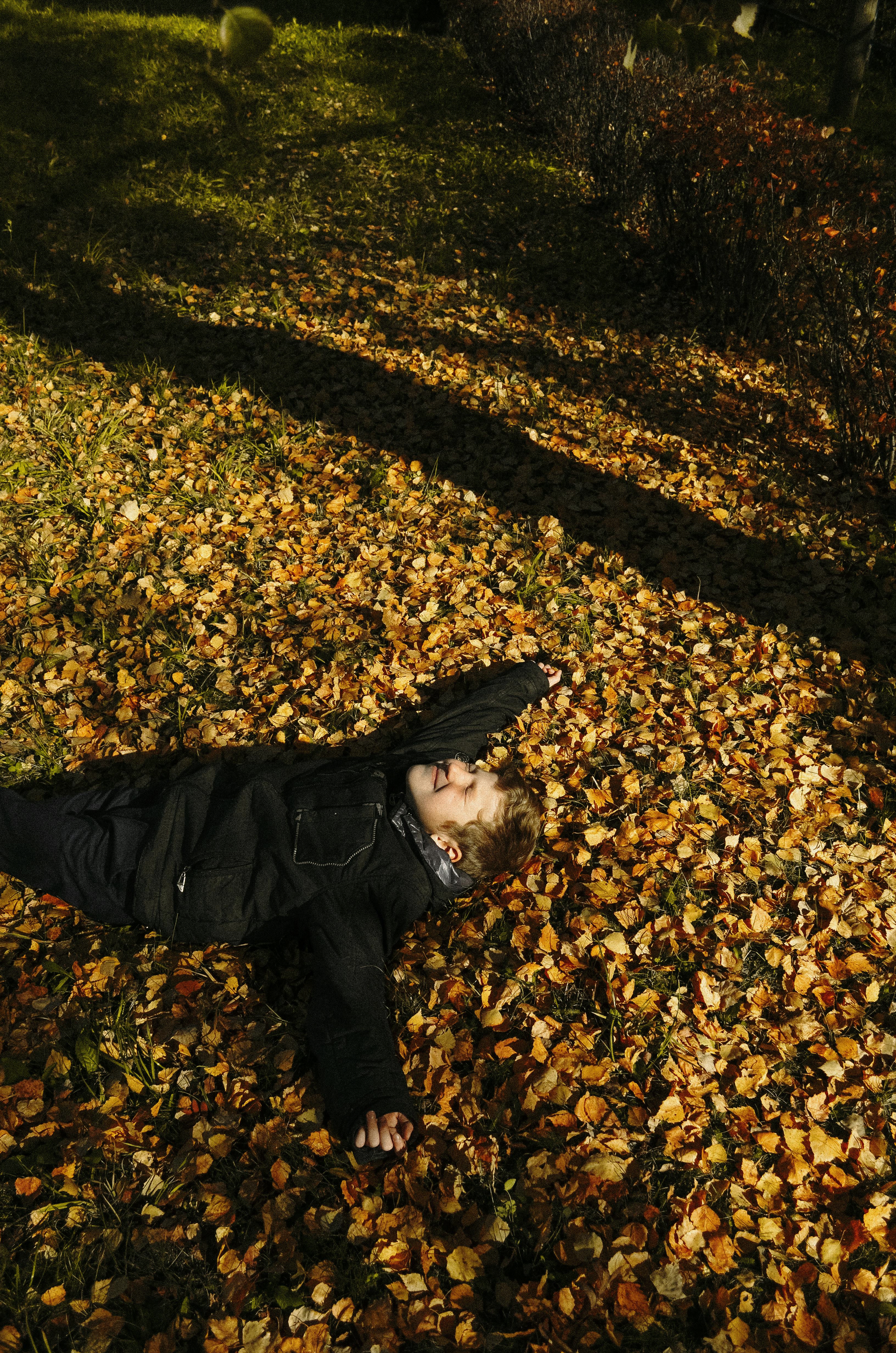 A man in a jacket lies peacefully on fallen autumn leaves, immersed in nature.