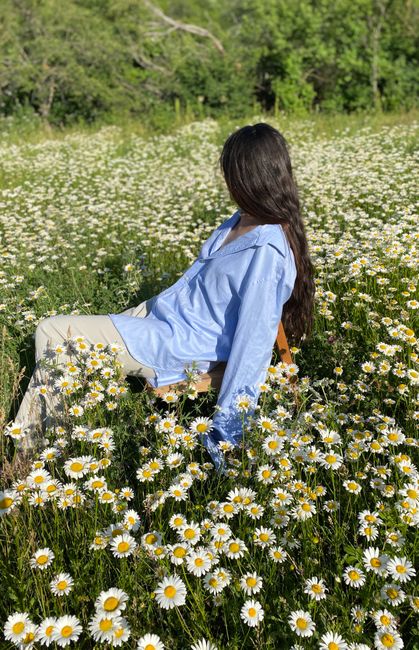 A serene outdoor scene of a woman sitting in a lush daisy field, embracing nature's beauty.