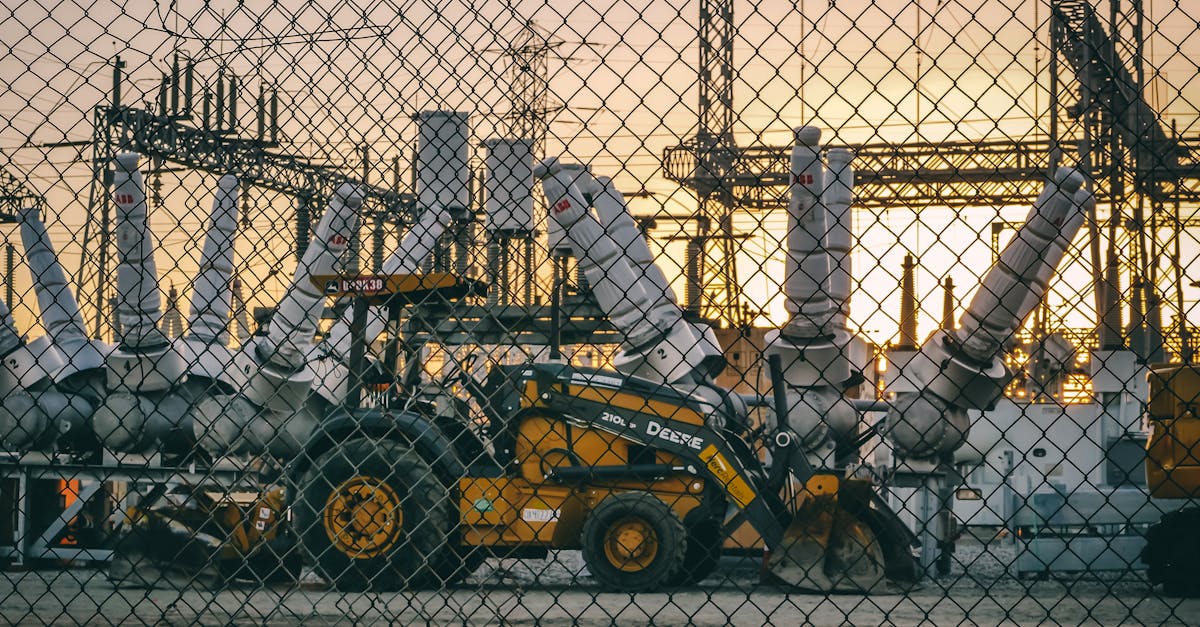 An industrial power plant with heavy machinery and equipment behind a chain link fence during sunset, showcasing energy infrastructure.