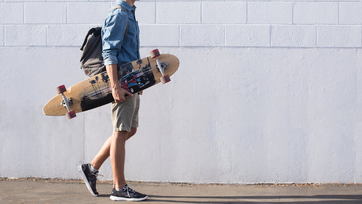 Free Man In Blue Top Carrying A Longboard Stock Photo