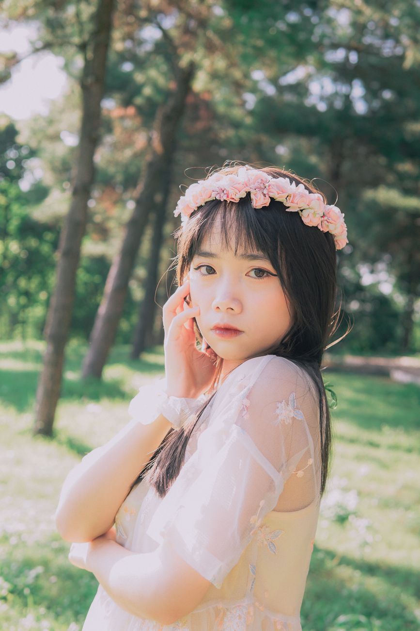 A young woman in a floral headband poses outdoors in a sunlit park, embodying natural beauty and ser