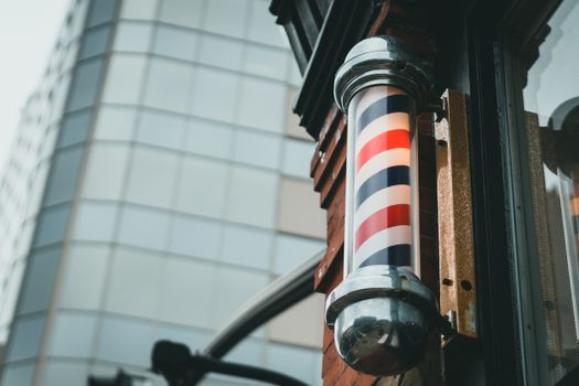 A retro barber pole mounted on a city building facade, symbolizing traditional barbering.