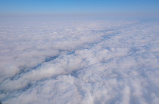 A tranquil aerial shot of a cloudscape with soft white clouds under a clear blue sky.