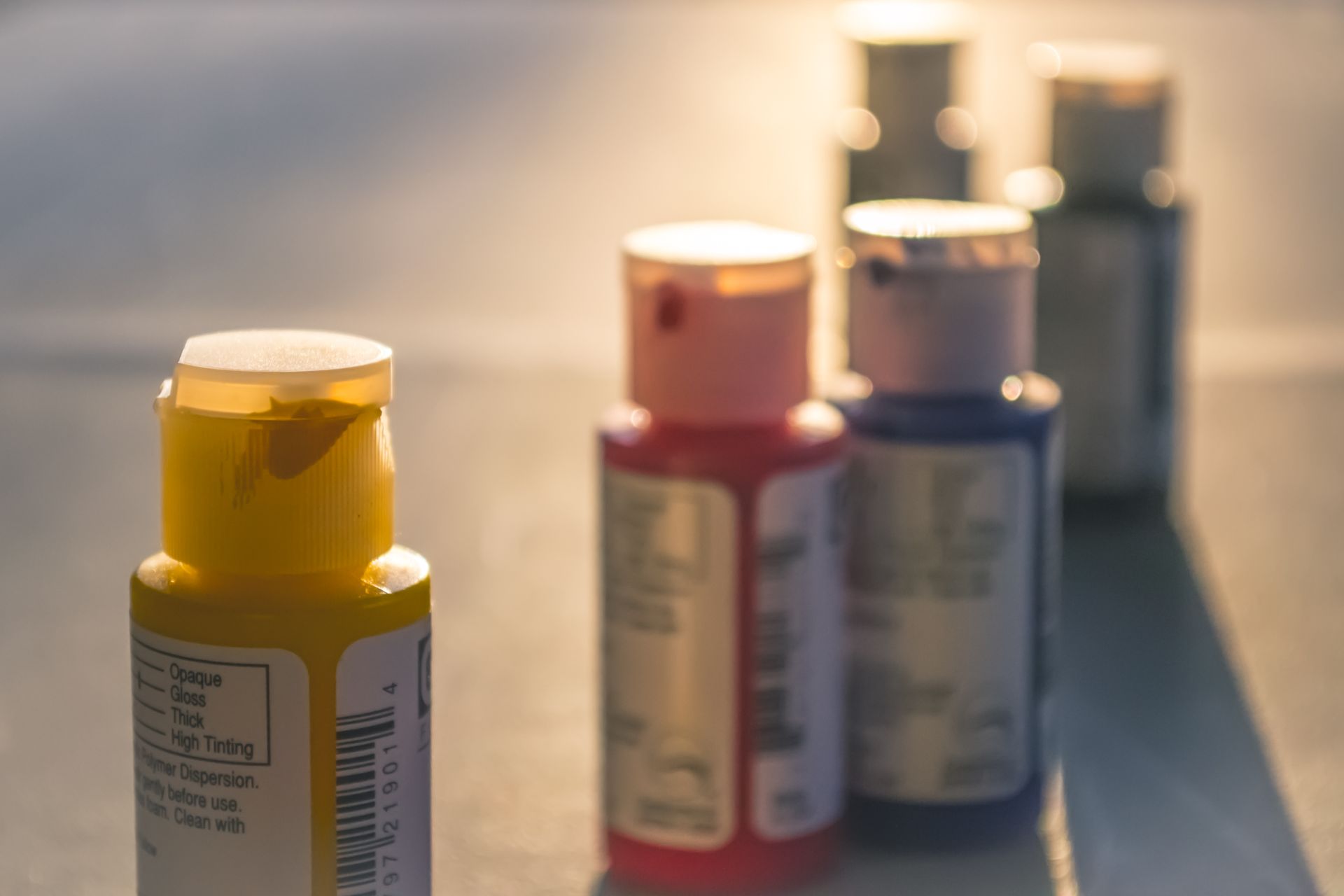 Close-up view of acrylic paint bottles in sunlight, highlighting vibrant primary colors.