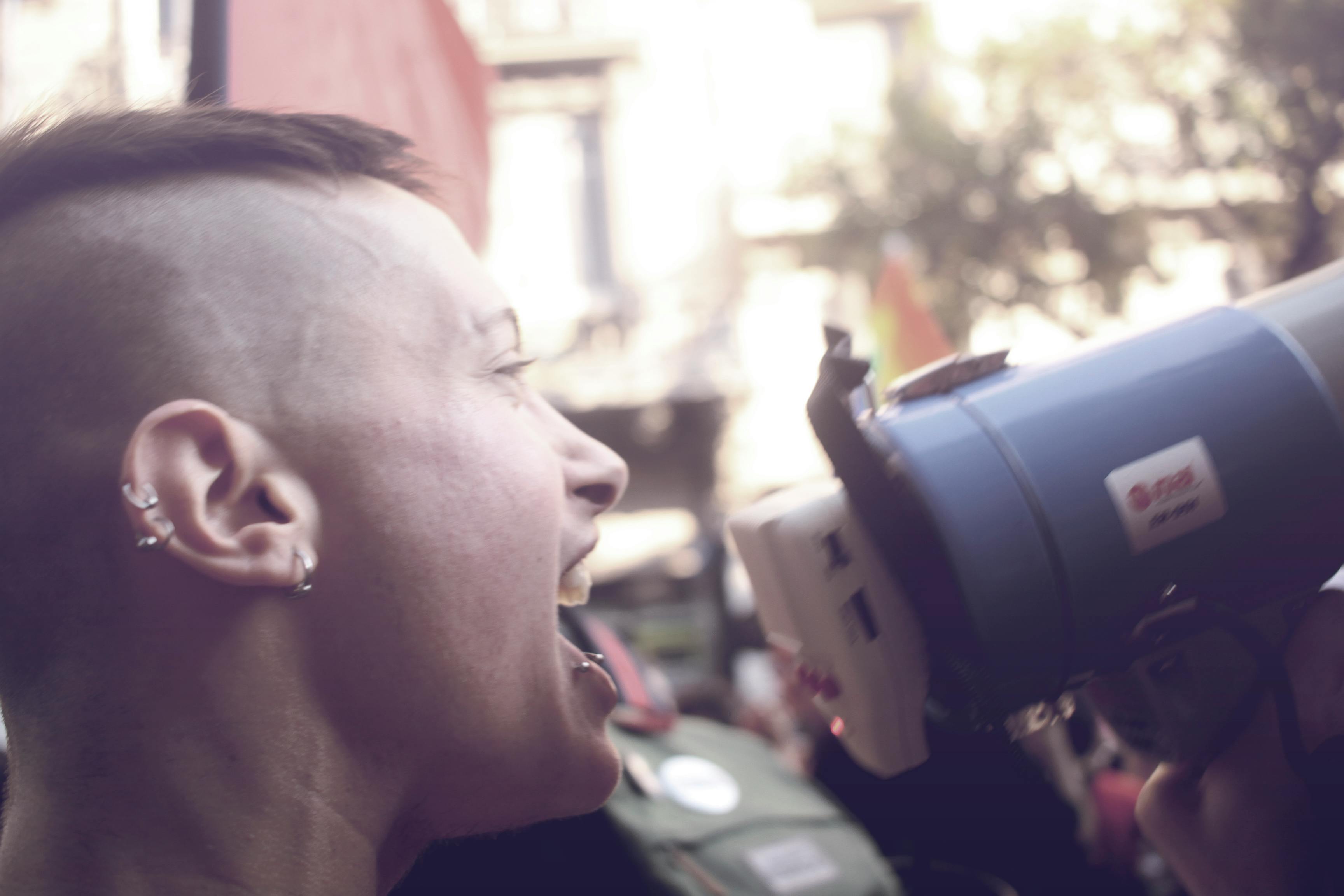Side view of a person passionately shouting into a megaphone at an outdoor protest.