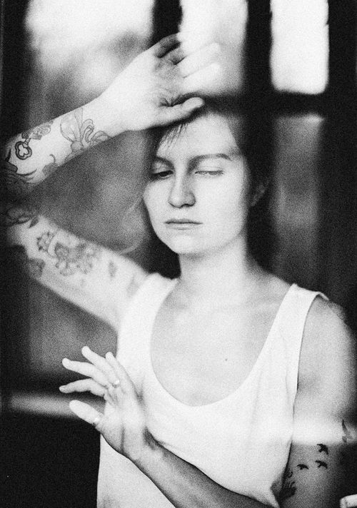 Free Black and white portrait of a tattooed woman in a reflective, introspective pose through a window. Stock Photo
