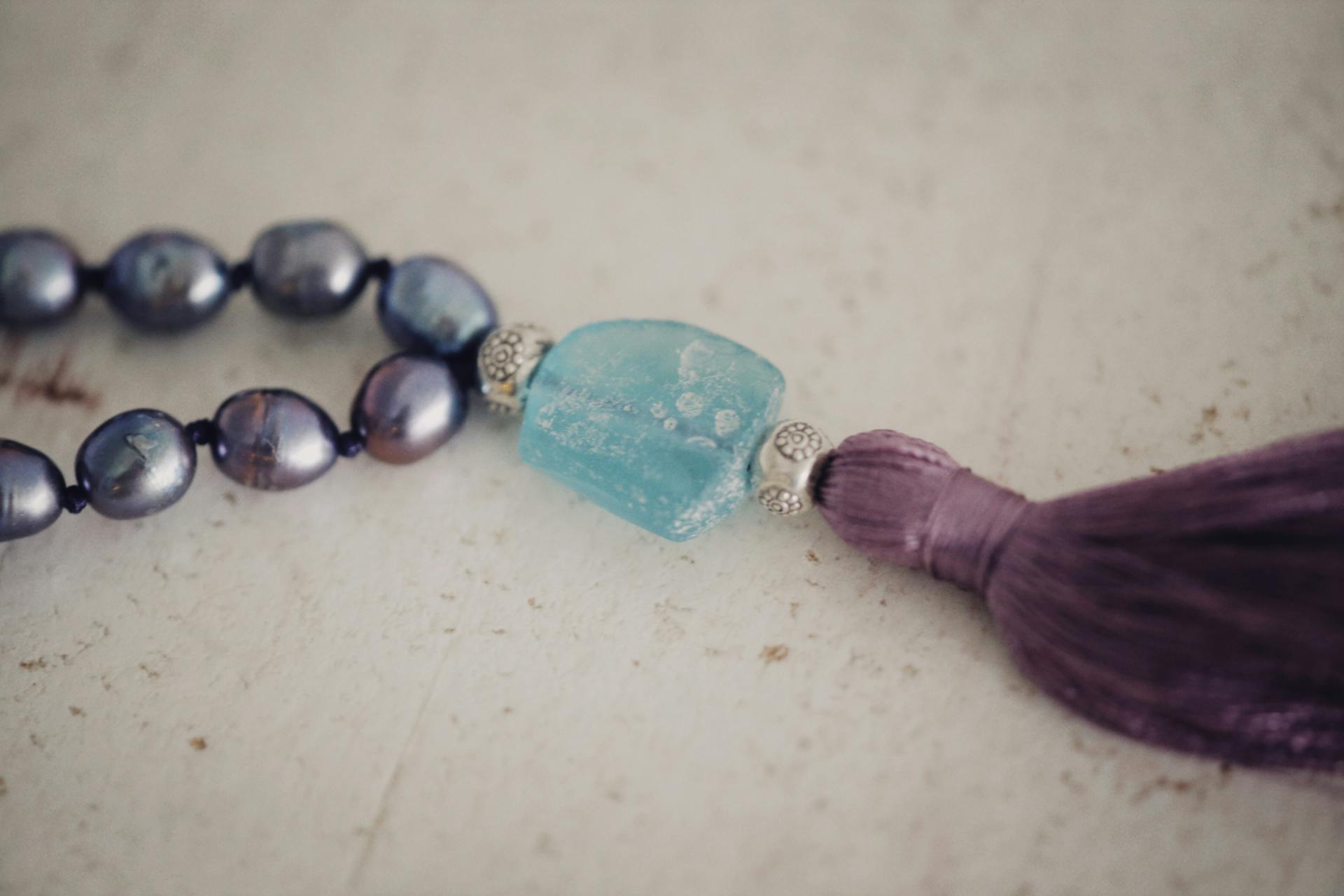 Close-up of a beaded necklace featuring a blue stone pendant and purple tassel.