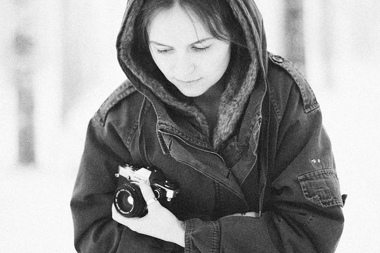 Hooded Woman In Winter Jacket Holding Camera Close To Her Body