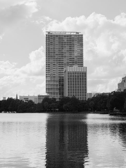 Black and white photo of a city's skyscraper reflecting in a calm lake.