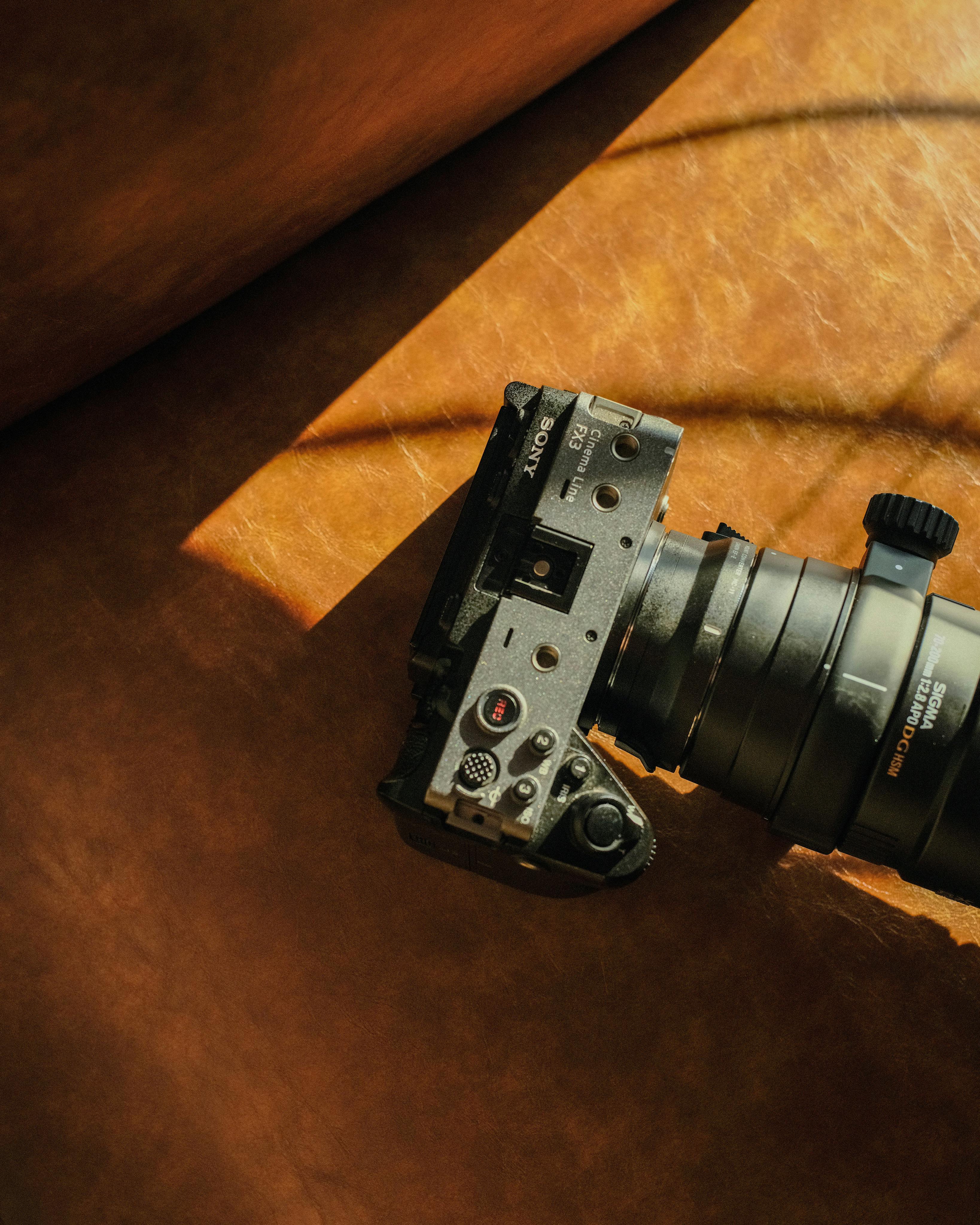 Top-down view of a modern mirrorless camera with lens on a leather surface in sunlight.