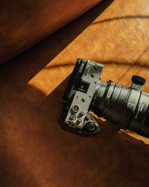 Top-down view of a modern mirrorless camera with lens on a leather surface in sunlight.