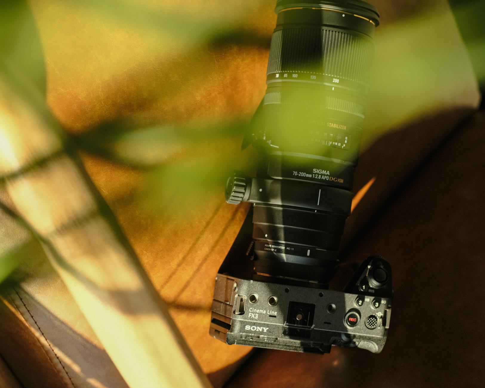 Camera with Sigma lens on a leather surface, highlighted by sunlight and plant shadows.