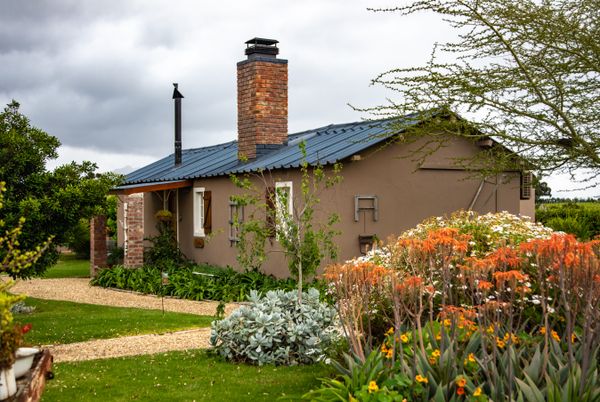 Rendered cottage with a brick chimney and a flowering front garden — photo by Magda Ehlers on Pexels