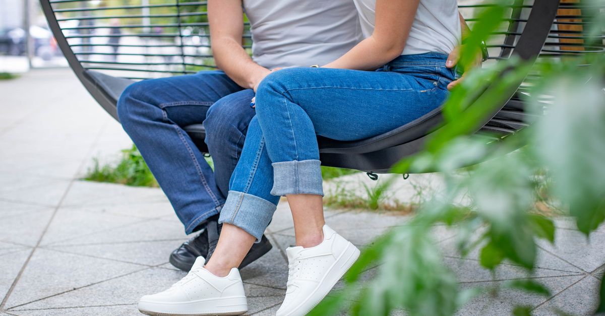A couple in jeans and sneakers casually sitting on a modern swing outdoors.