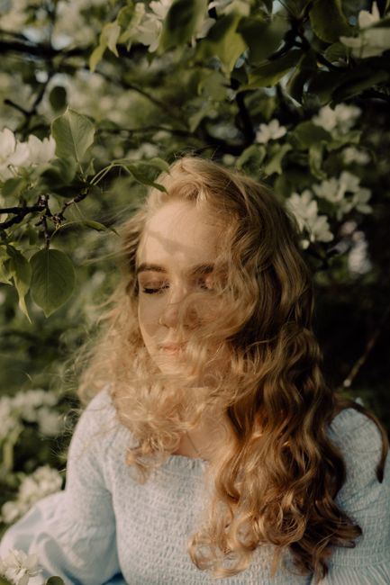 A serene moment of a woman with wavy blonde hair amidst lush green foliage in spring.
