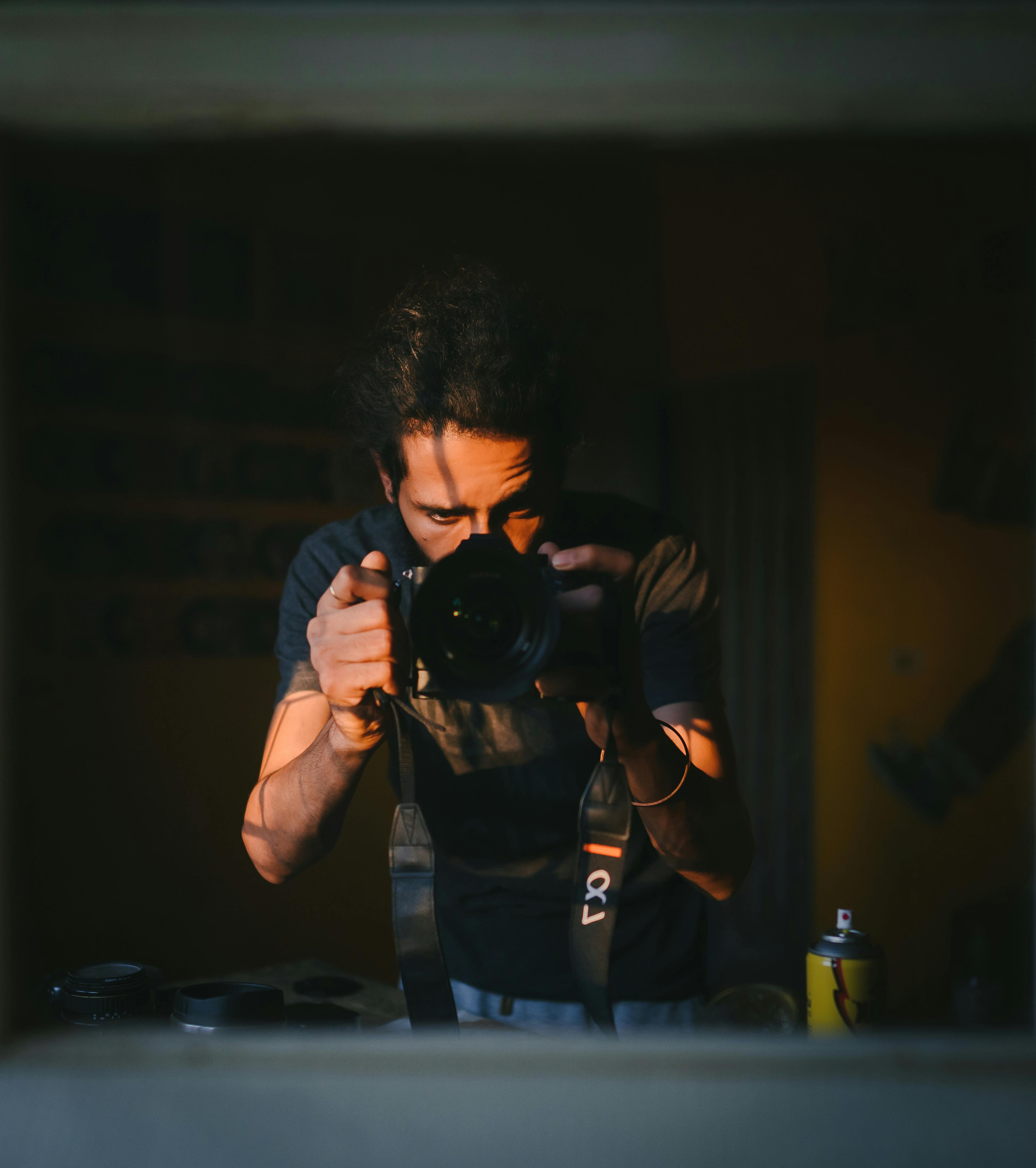 Free Photographer taking a photo in warm lighting indoors, emphasizing creative shadow and light play. Stock Photo