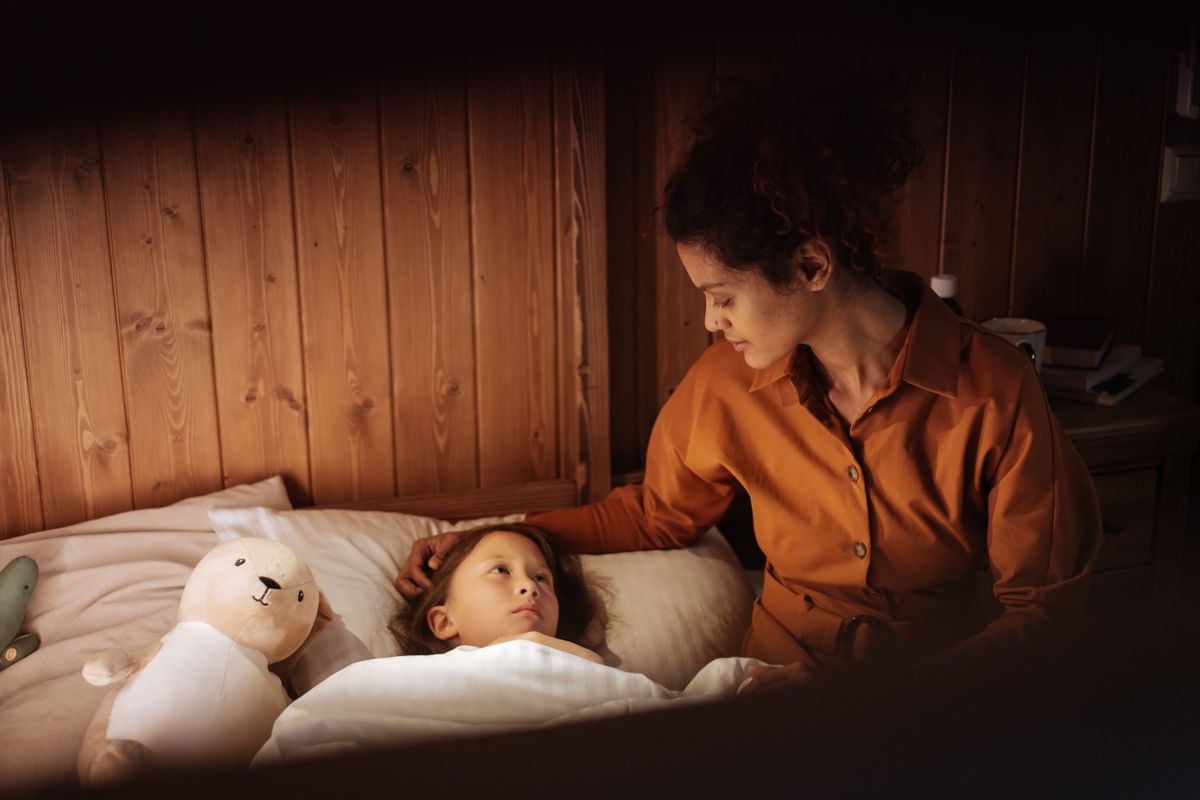 Une maman borde tendrement son enfant dans son lit le soir