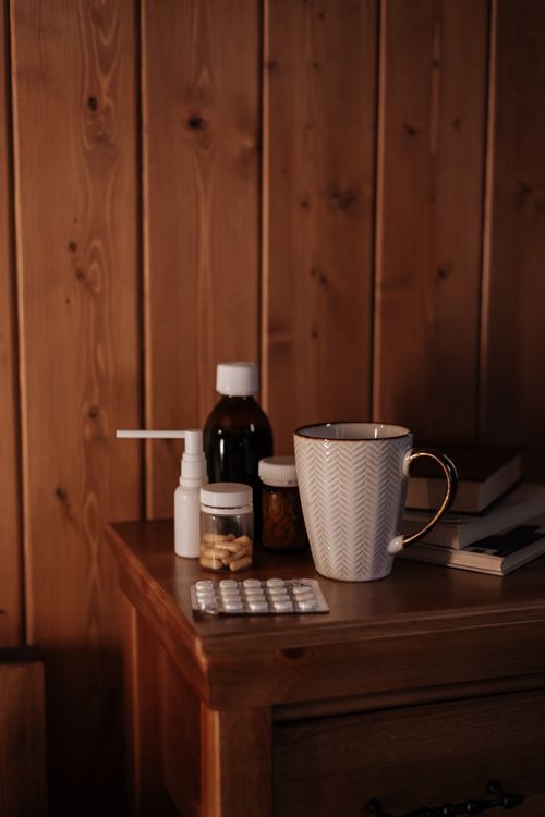 Free Wooden table with medicine, a mug, and books in a cozy room setting, ideal for themes of home care and wellness. Stock Photo
