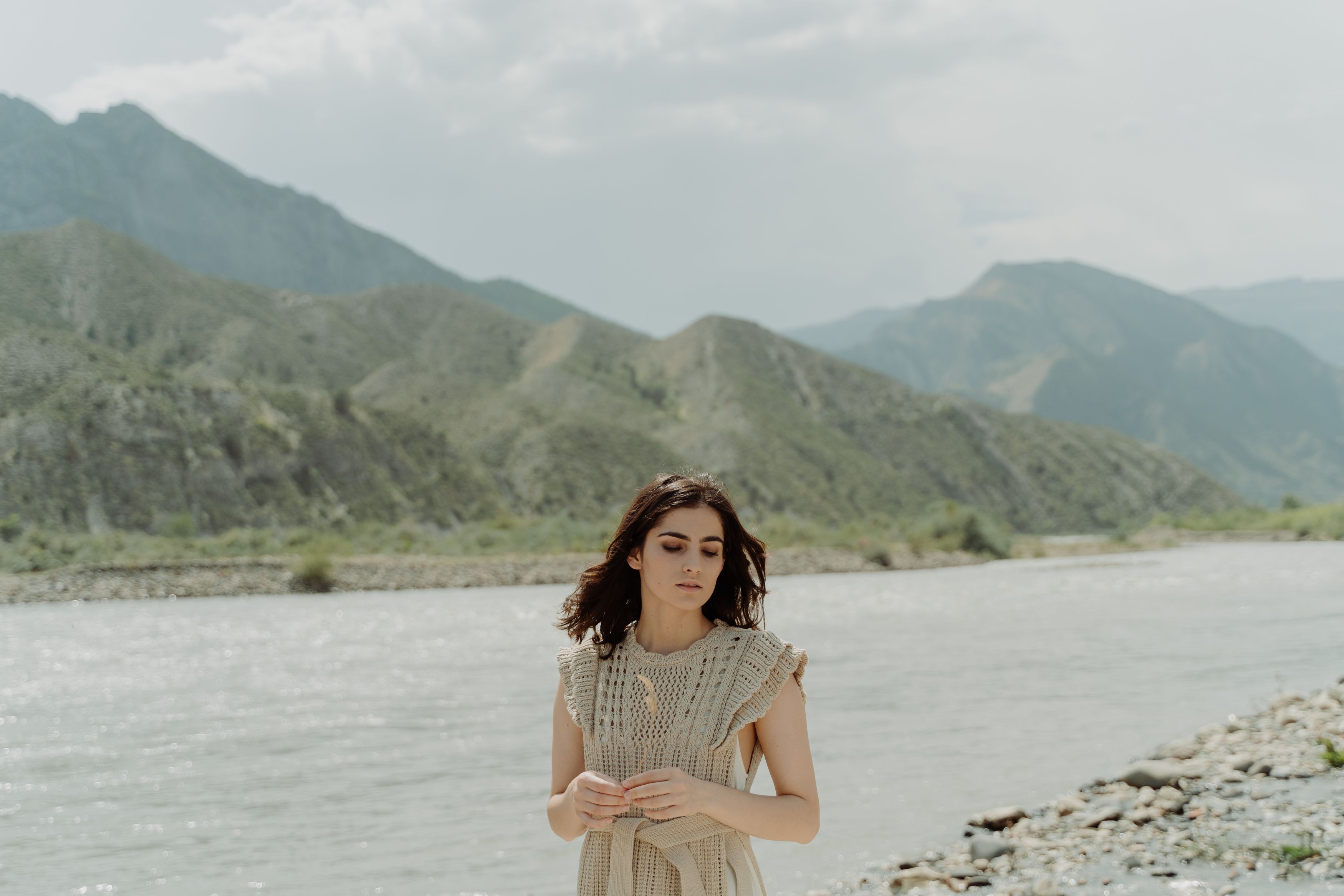 Young woman with closed eyes by a river amidst scenic mountains in summer.