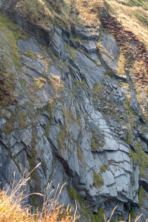 Free Sharp rocky cliff with distinct geometric formations and light vegetation growth. Stock Photo