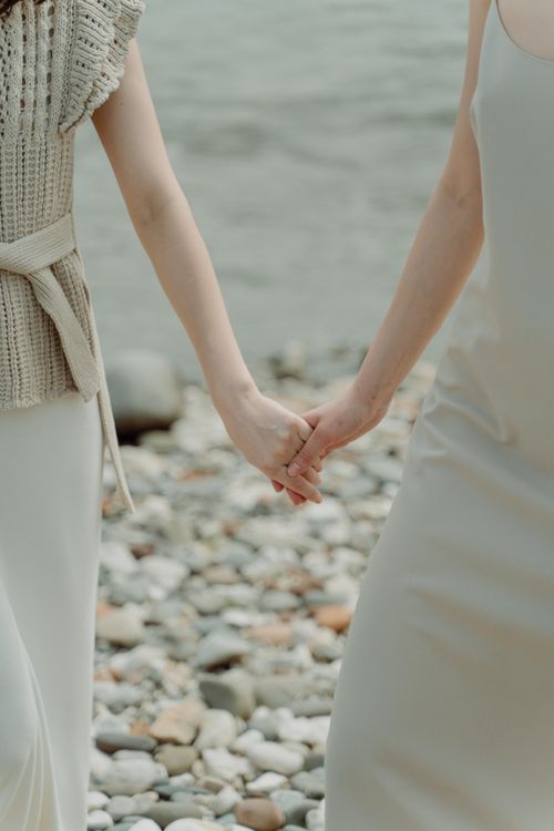 Free Close-up of two people holding hands by a rocky waterfront showcasing love and connection. Stock Photo