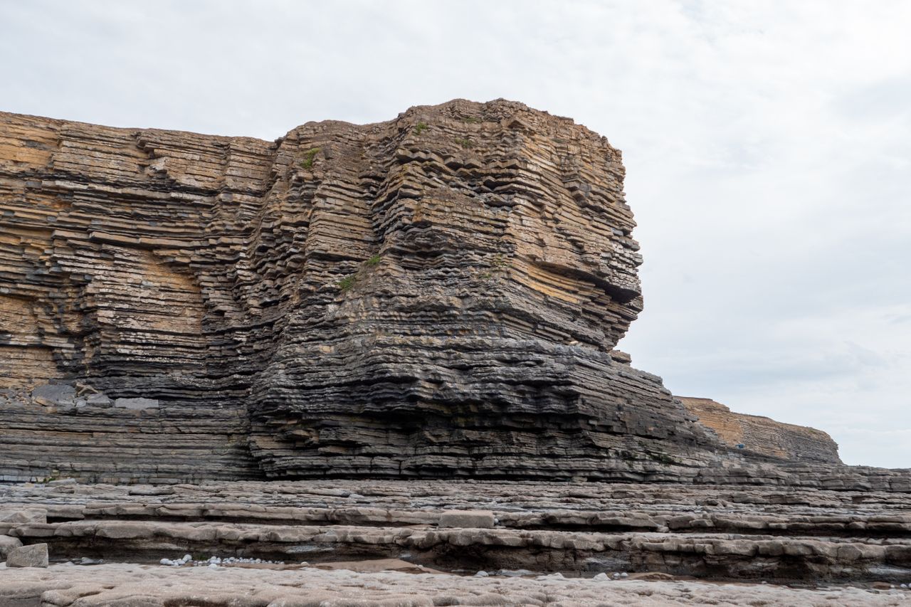 Dramatic rocky cliff with layered formations under an overcast sky, capturing rugged nature's beauty.