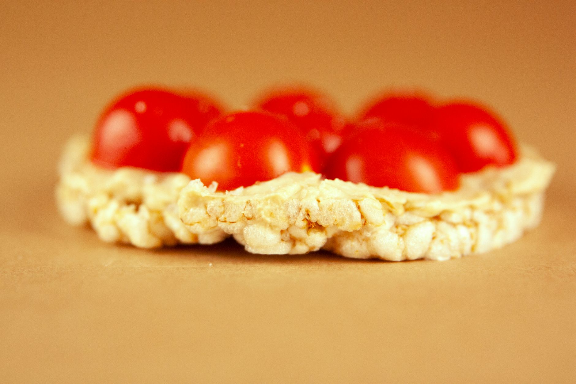 Macro shot of a rice cake topped with fresh cherry tomatoes on a warm background.