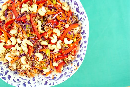 Colorful quinoa salad with cashews, peppers, and cabbage in a decorative bowl on a turquoise background.