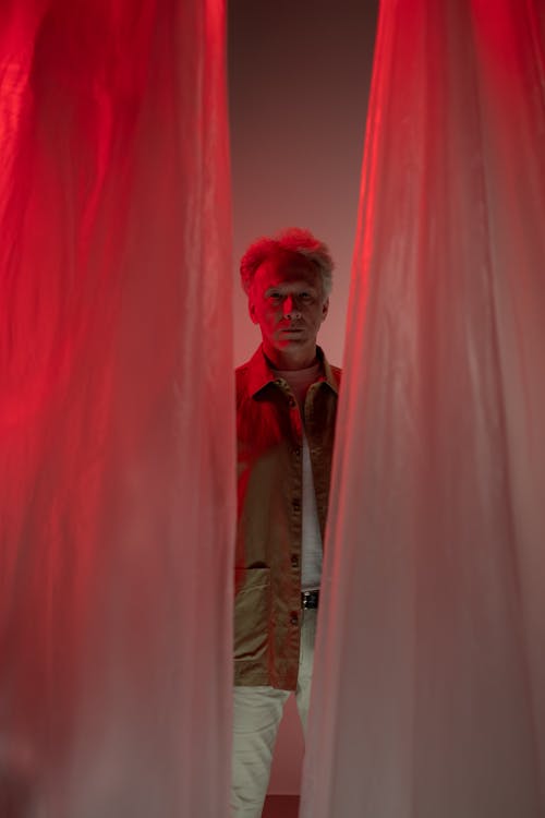 Elderly Man Standing behind Red Curtain