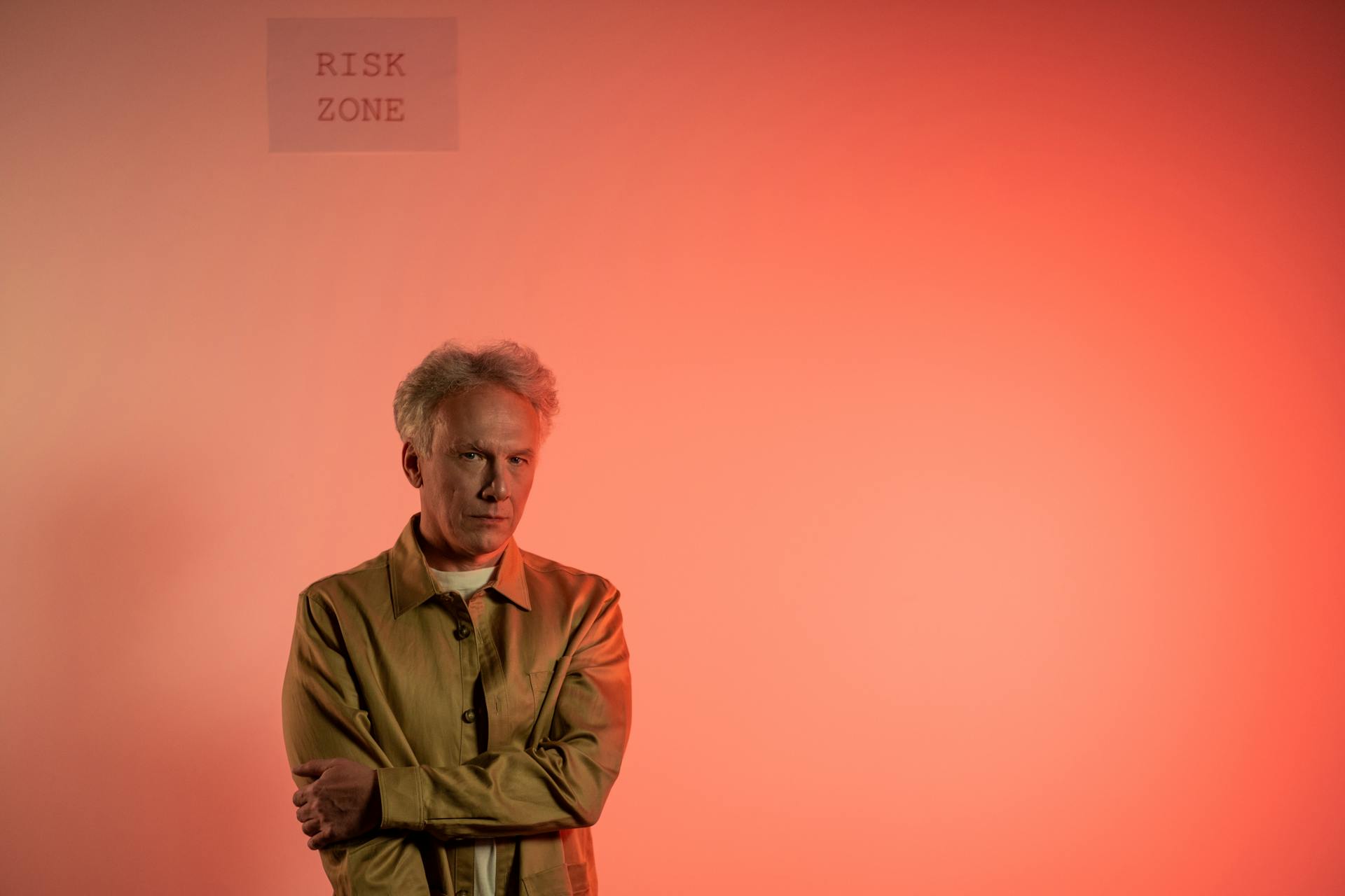 Elderly Man Standing below Risk Zone Warning on Wall