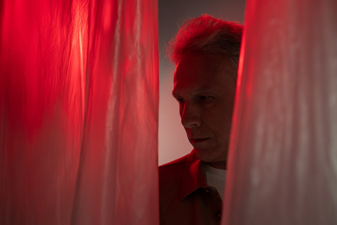 Elderly Man Looking Right behind Red Curtain
