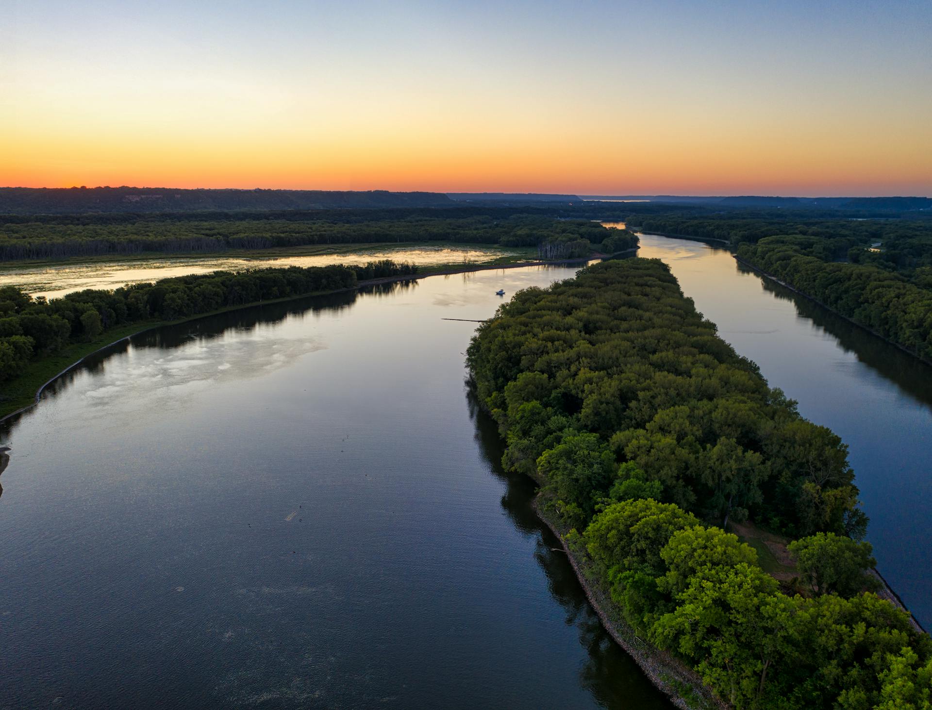 A dramatic aerial shot of the Mississippi River surrounded by lush greenery during sunset.