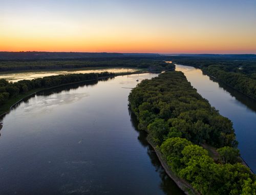 Free A dramatic aerial shot of the Mississippi River surrounded by lush greenery during sunset. Stock Photo