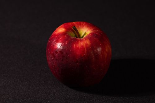 Free A fresh, shiny red apple with water droplets against a dark backdrop, symbolizing health. Stock Photo