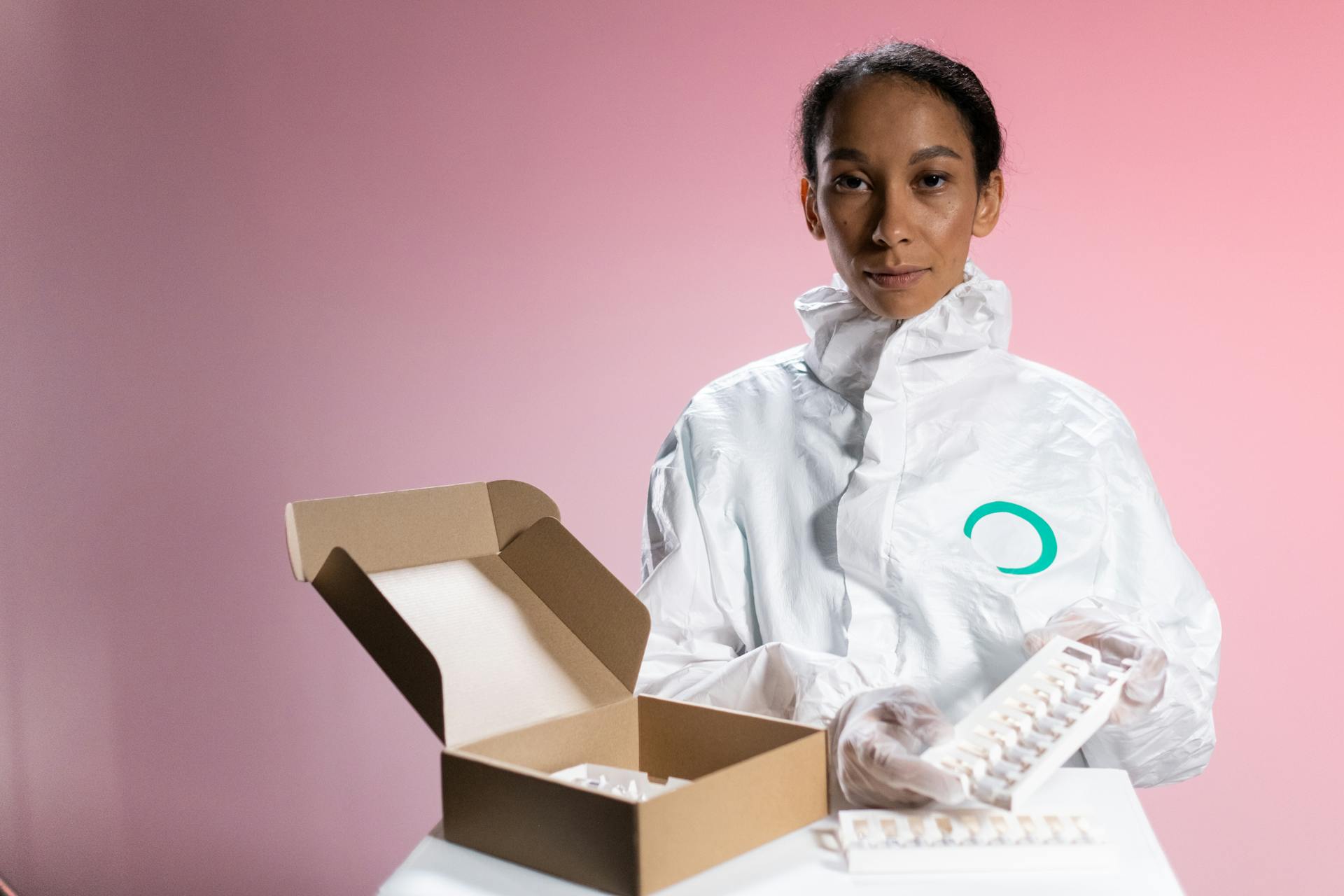 A Female Nurse Looking At Camera and Holding A Box with Vaccines